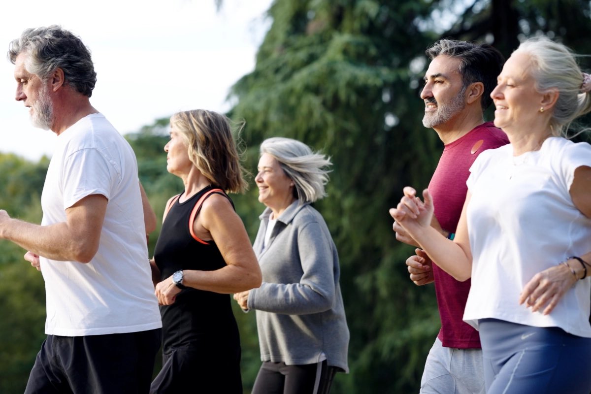 Five runners in their fifties and sixties running together through a park in daylight