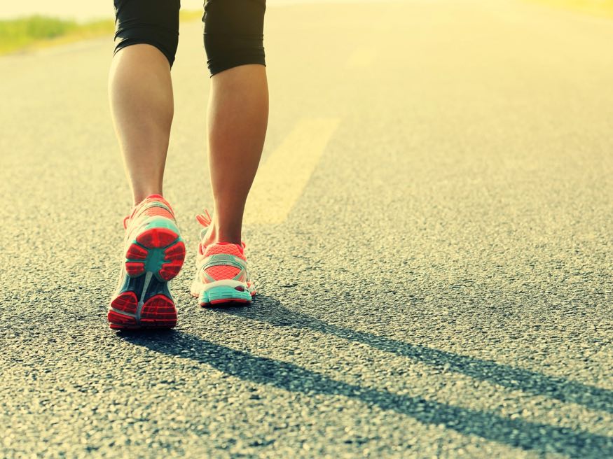A runner's legs and shoes on an empty road in the morning sun
